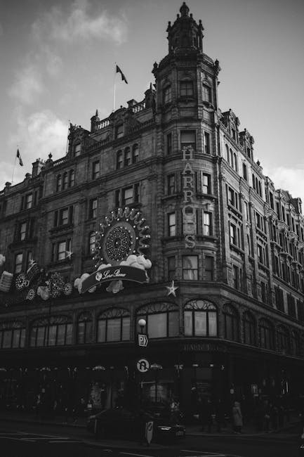 A black-and-white photograph of a historic multi-storey building located in Knightsbridge, featuring ornate architectural details and a prominent marquee signage. The building has large windows, decorative stonework, and a rounded corner tower with a flagpole on top. In front of the building, there is a street with parked vehicles and pedestrians. The scene captures the urban environment during daytime, with overcast skies casting diffused light. This setting illustrates the typical exterior of a property where professional removals and home relocation services, such as those provided by [COMPANY_NAME], may facilitate furniture transport and moving logistics while complying with local council rules and permits for removals in the area.