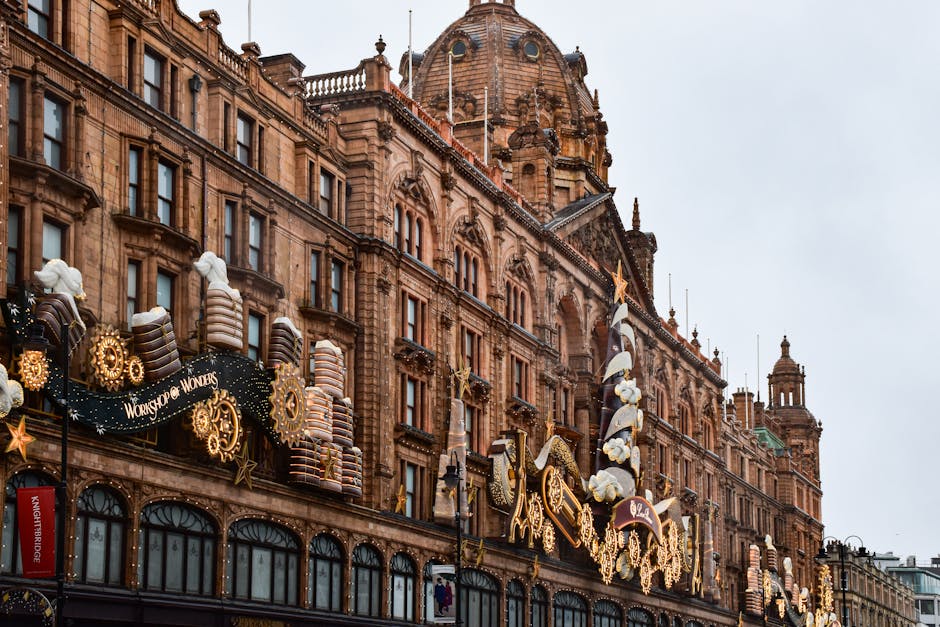 A detailed exterior view of a historic building in Knightsbridge during the daytime, featuring ornate architecture with brownstone facades, arched windows, and decorative columns. The building is decorated with festive holiday lights, including illuminated stars, snowflakes, and various themed ornaments, possibly for Christmas or winter celebrations. The decorations are attached to the facade and extend onto light poles. The sky is overcast, creating diffuse lighting that highlights the textures of the stonework and decorations. This setting reflects the area's vibrant commercial and residential environment, which may be subject to street closure rules during special events or moving procedures. The image emphasizes the importance of careful home relocation planning in such busy and historic locations, where coordination with local council regulations is often necessary for smooth furniture transport and packing during house removals. Consequently, [COMPANY_NAME], specializing in removals within this area, supports clients in managing logistics for house moves and transport within densely decorated and regulated streets like those in Knightsbridge.